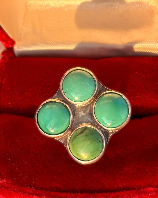 A silver ring with four round light green turquoise cabochons arranged in a flower shape