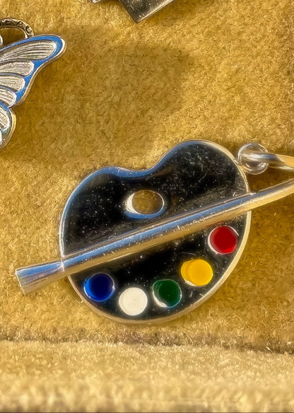 Three vintage silver charms including a butterfly, 'My Diary' book, and paint palette on a velvet background.