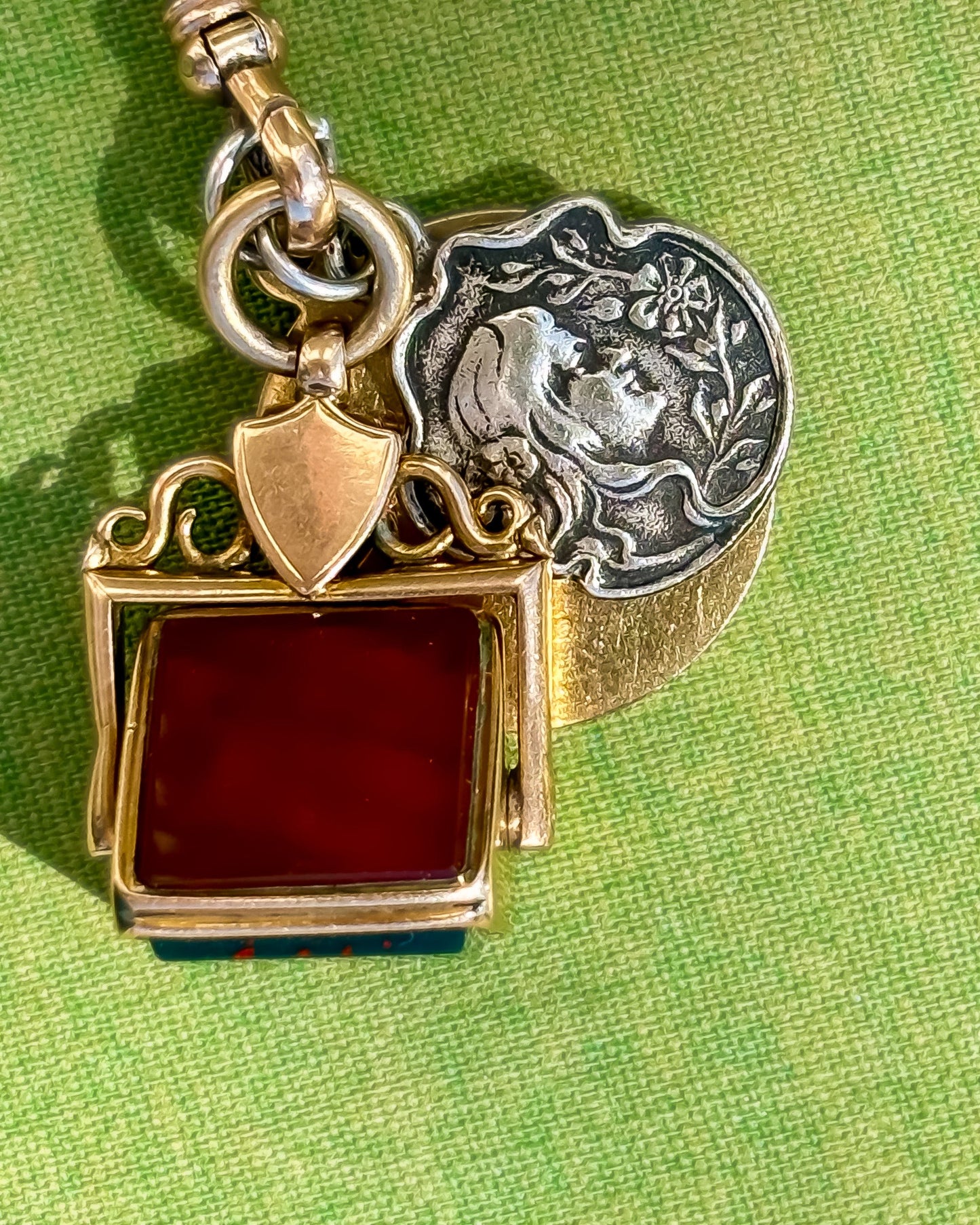 Gold fob pendant with carnelian gemstone on a green fabric background