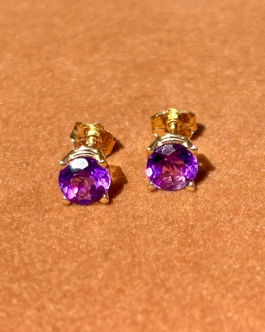 Pair of gold earrings with amethyst gemstones on a brown background