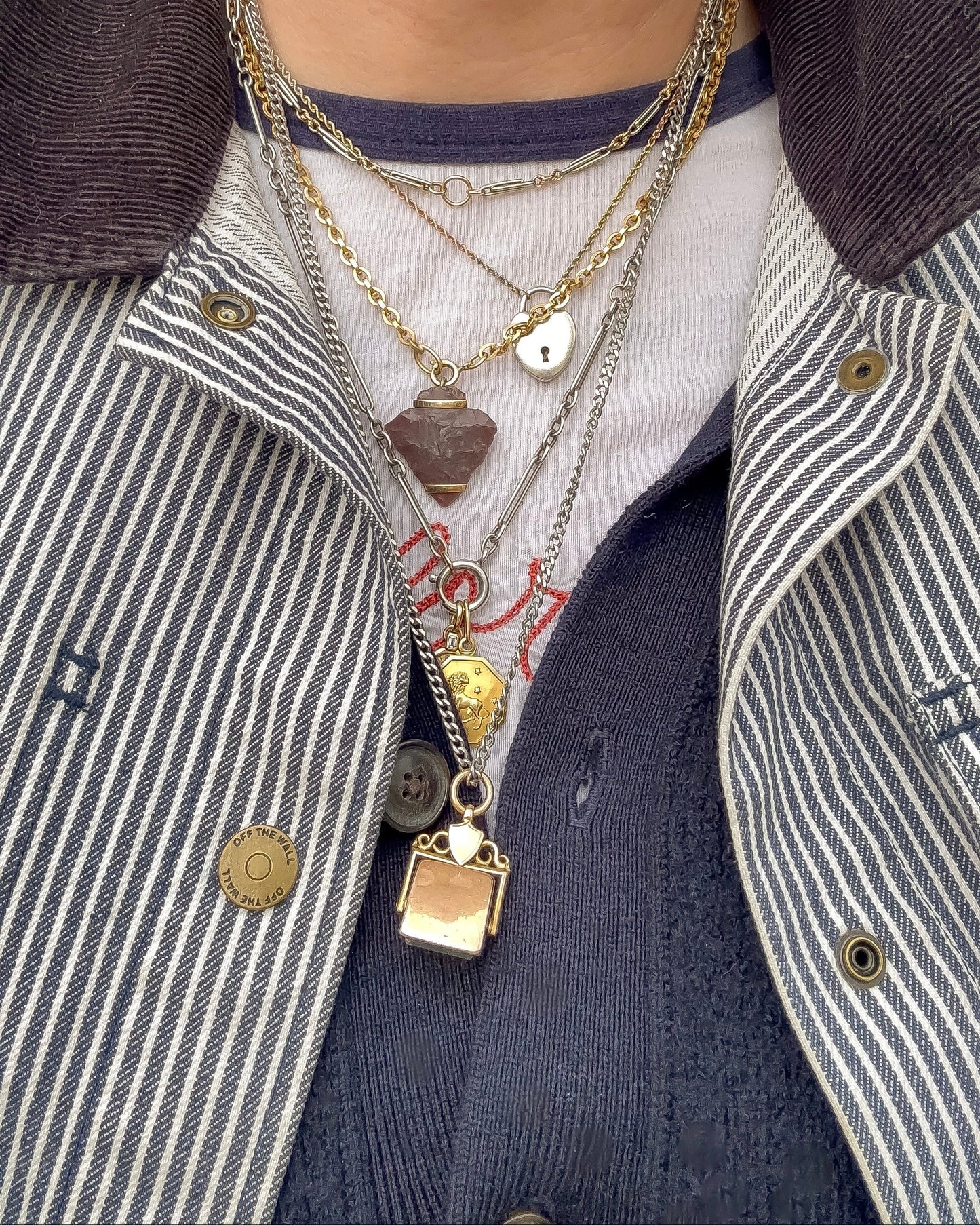 Close-up of layered necklaces with various vintage and antique pendants on a striped shirt and jacket.