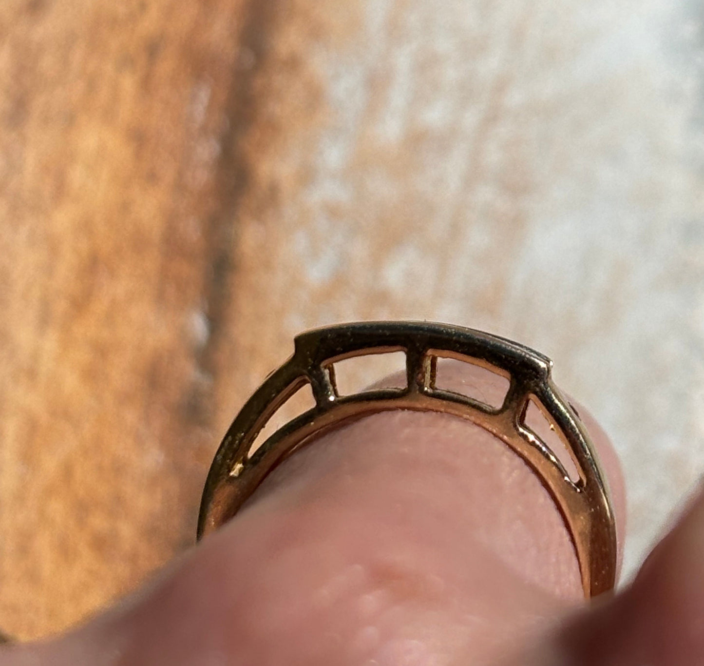 Close-up of a hand wearing a gold ring on a blurred background.