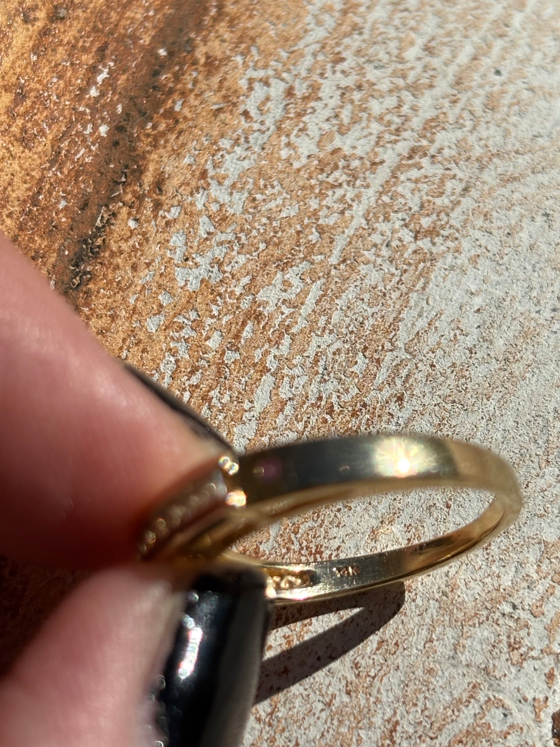 Vintage 14K gold ring being held between fingers on a textured surface