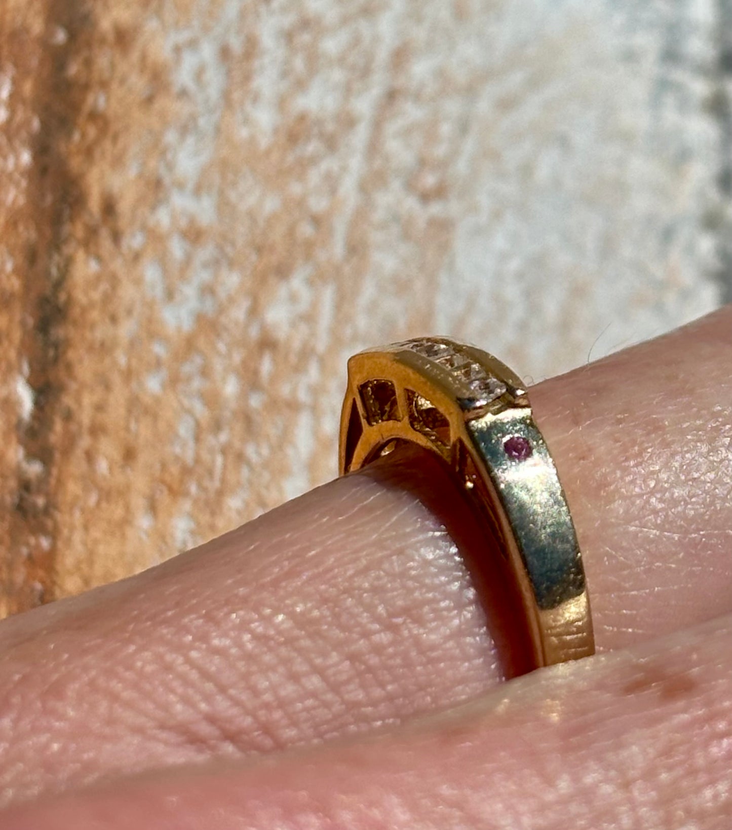 Yellow gold ring with diamonds on a finger against a textured background