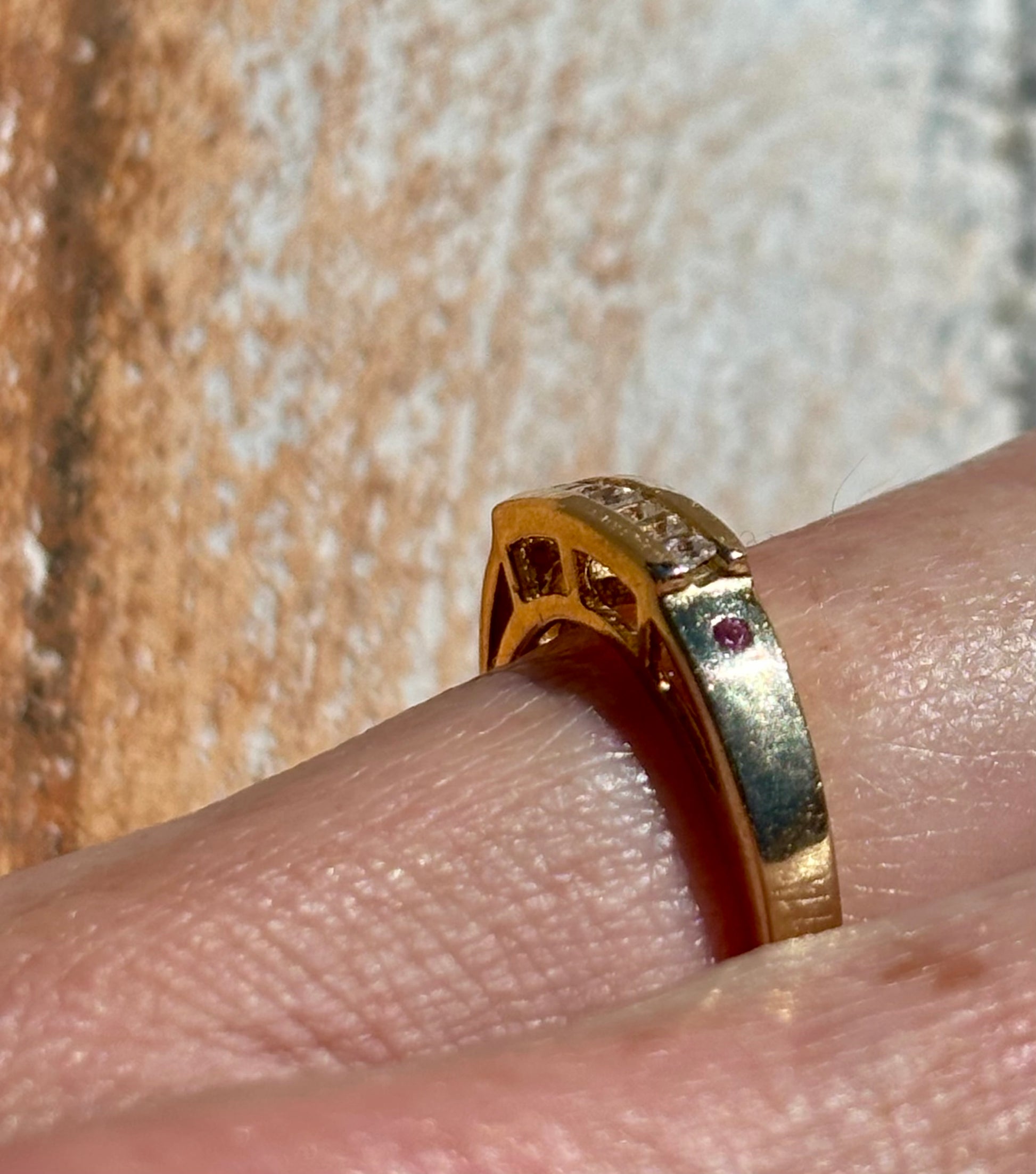 Yellow gold ring with diamonds on a finger against a textured background