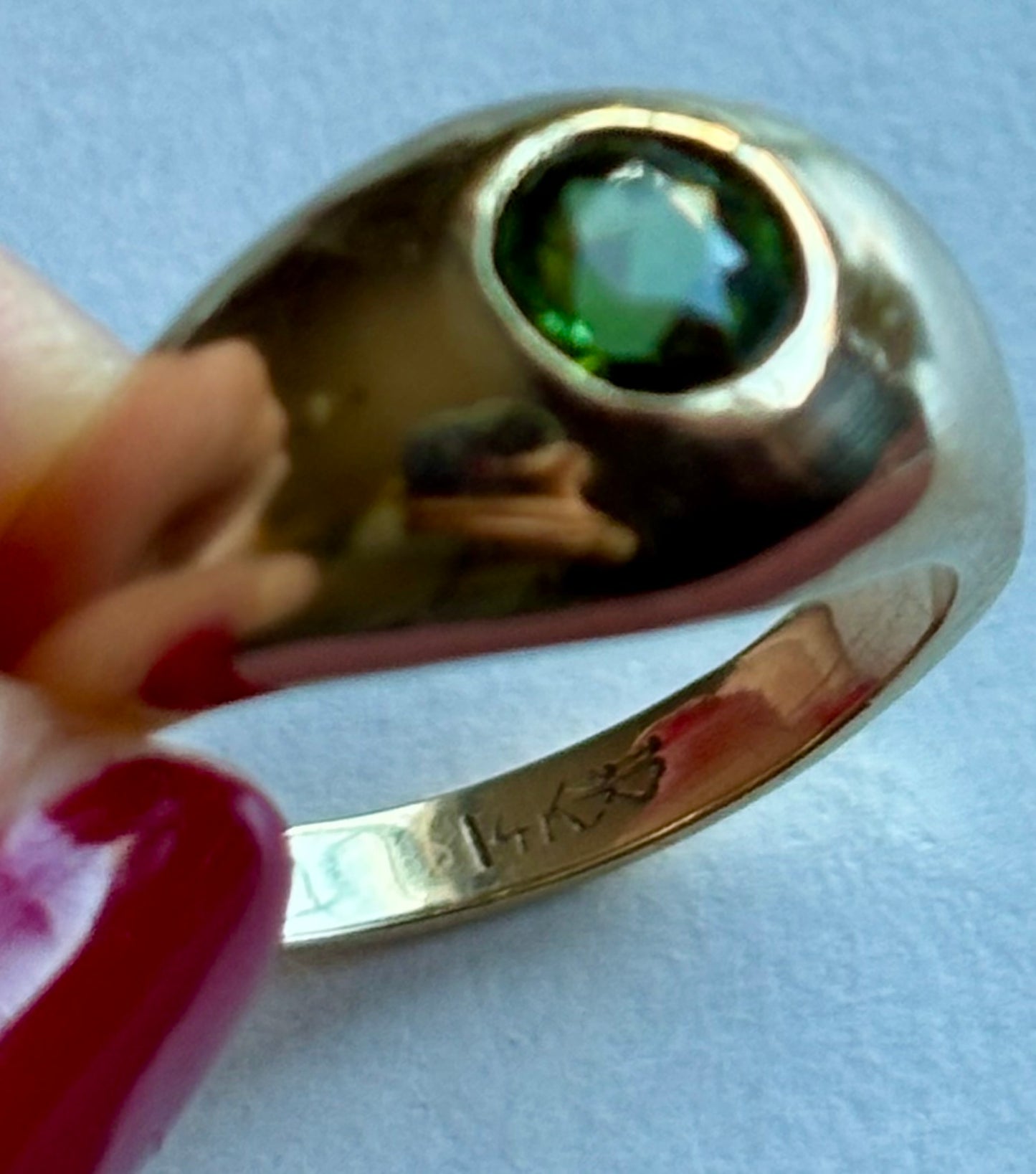 Gold ring with a green gemstone held by a hand on a light background